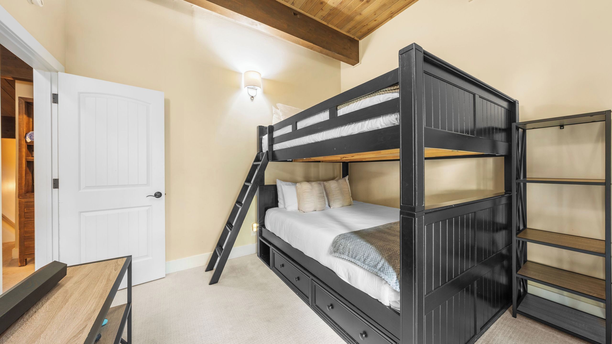 A bunk bed with a ladder, a white door, and a shelf unit.