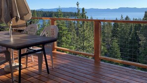 Una terraza de madera con una mesa y sillas, con vista a un lago y montañas.