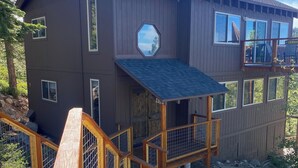 Una cabaña de madera de dos pisos con un balcón, una chimenea y una escalera de madera que lleva a una terraza.