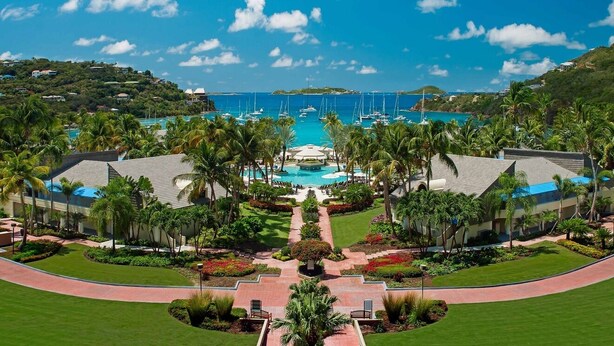 Un resort con piscina central, palmeras y vista al océano.