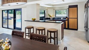 Una cocina moderna con una isla central, taburetes de bar y un comedor con mesa y sillas.