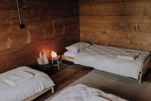 A cozy wooden room with a bed, a small stool, and a table with a candle.