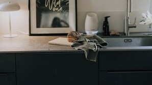 A kitchen with a framed sign that reads "Wild Ones," a loaf of bread, a cloth, a soap dispenser, and a faucet.