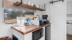 A compact kitchen with a wooden countertop, a built-in microwave, and a sink. A window reveals a view of trees and a vehicle outside. - Starlight Streamer - Cozy Airstream Escape in Williams, AZ (Williams)