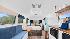A compact RV interior with a bed, seating area, kitchenette, and a window offering a view of the outdoors. - Starlight Streamer - Cozy Airstream Escape in Williams, AZ (Williams)