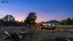 Een rustieke buitenruimte met houten meubels en een vintage caravan met verlichting.