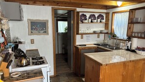 A compact kitchen with a stove, sink, and wooden cabinets. There is a small dining area with a table and chairs. - 1 Bedroom Vacation Cottage in San Marcos/Wimberley, TX (San Marcos)