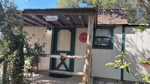 A rustic cabin with a wooden deck, a green door, and a sign reading "Passion Flower." - 1 Bedroom Vacation Cottage in San Marcos/Wimberley, TX (San Marcos)