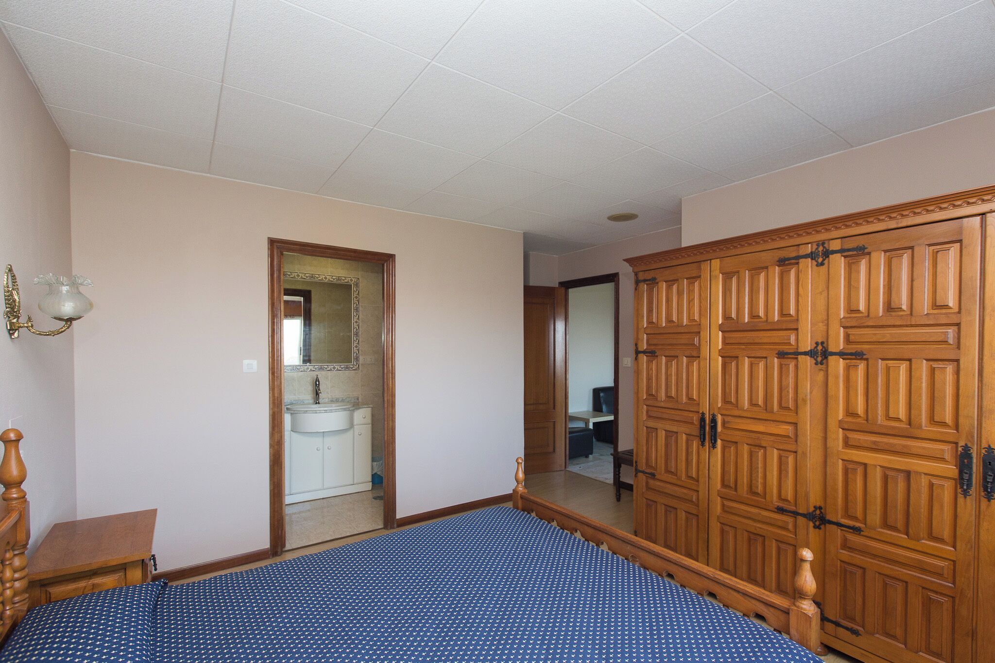 A bedroom with a bed, wooden wardrobe, and a bathroom visible through an open door.