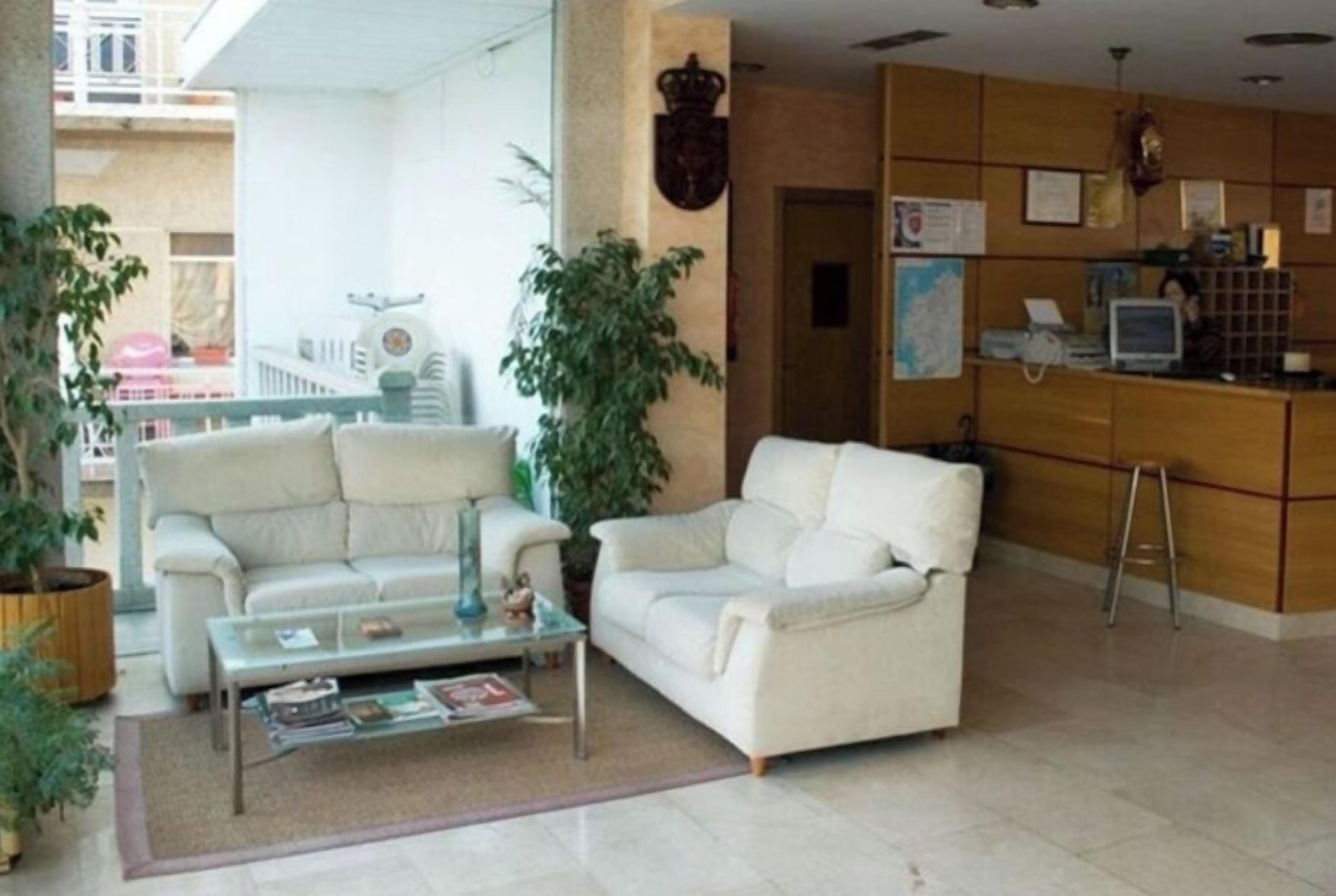 A living room with two white sofas, a glass coffee table, and potted plants.
