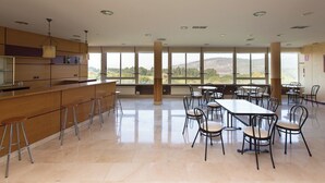 A spacious dining area with a long counter and multiple tables and chairs, large windows with a view of hills, and a modern ceiling design. - My Rooms City Hotel Monte Blanco (Neaño)