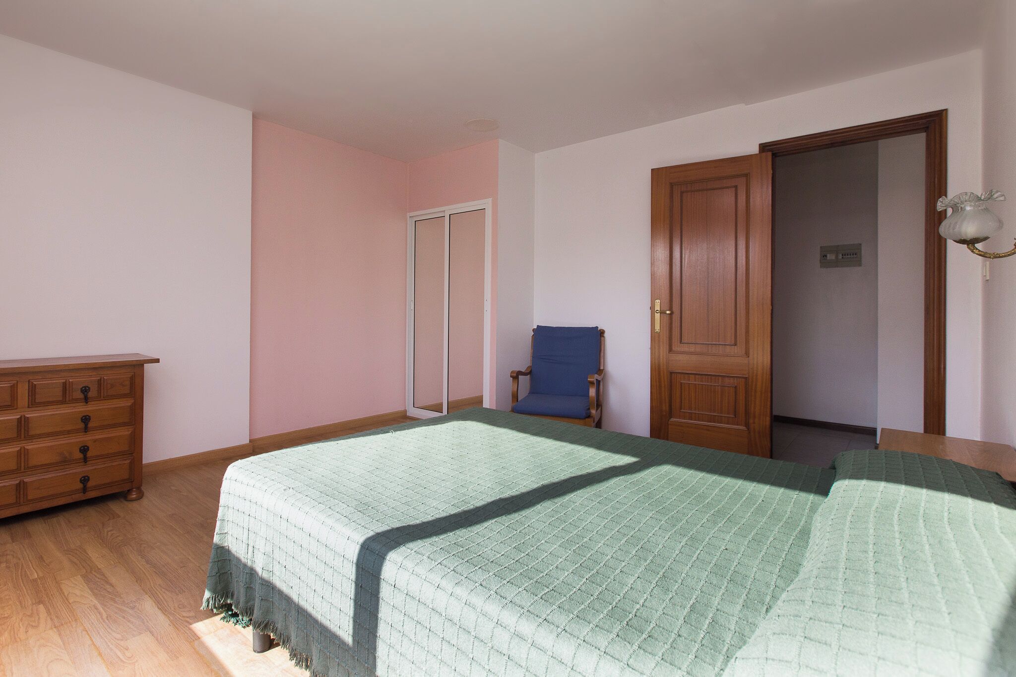 A bedroom with a bed, dresser, chair, and a door.