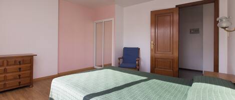 A bedroom with a bed, dresser, chair, and a door.