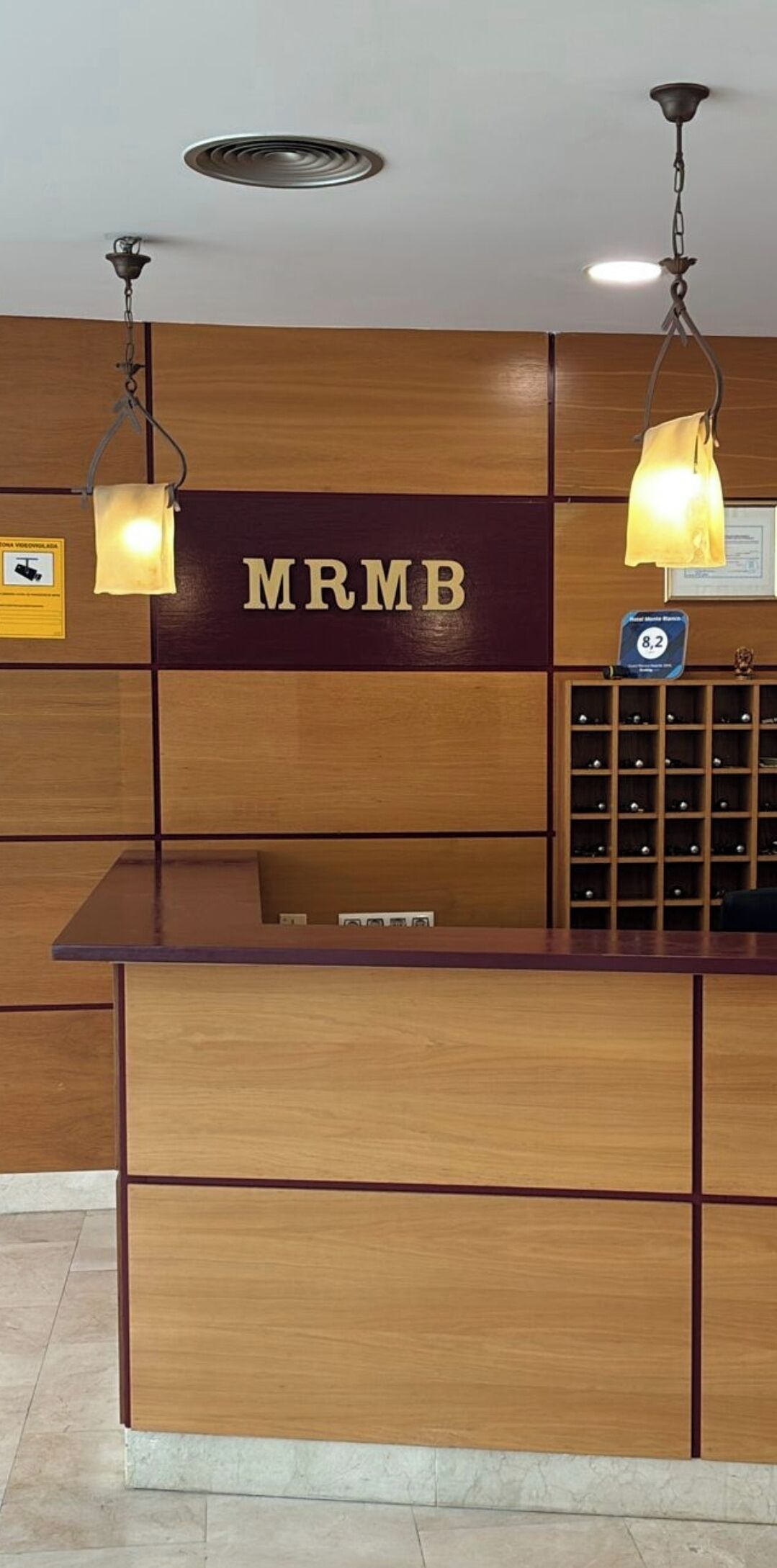 A reception desk with a sign reading 'MRMB,' overhead lighting, and a display of wine bottles.