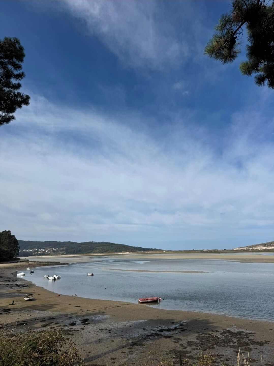 A coastal landscape with a sandy beach, calm water, and boats.