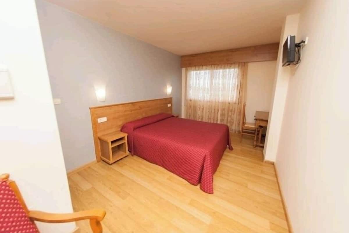Et lille, pænt indrettet soveværelse med en enkeltseng, et trænatbord, en stol og et lille bord.