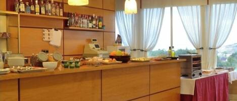 A buffet setup with a variety of food items and beverages, a cash register, and a view of the outdoors through large windows.