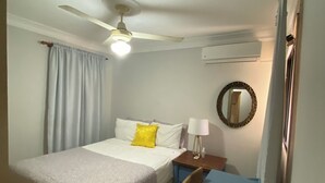 Een hotelkamer met twee bedden, een bureau, een stoel, een plafondventilator, een airconditioning en een spiegel aan de muur.