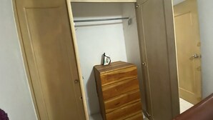 Een kamer met een houten garderobe, een klein houten kistje en een metalen stang.