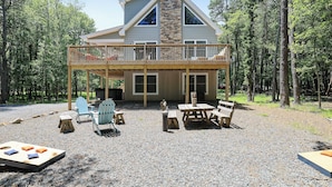 A two-story cabin with a deck, surrounded by a forest. - Hunt Hideaway, 4bd 3ba sleeps 12, hot tub, 85” TV, arcades! (Albrightsville)