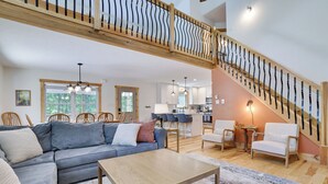 A spacious living area with a large sectional sofa, a wooden coffee table, and a staircase with a unique railing design. - Hunt Hideaway, 4bd 3ba sleeps 12, hot tub, 85” TV, arcades! (Albrightsville)