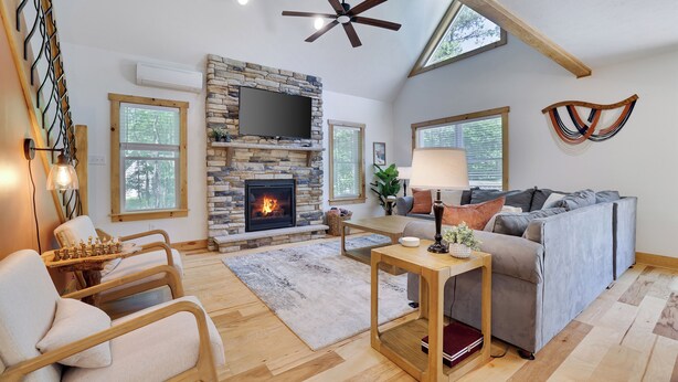 A spacious living room with a stone fireplace, a ceiling fan, and a large gray sofa. - Hunt Hideaway, 4bd 3ba sleeps 12, hot tub, 85” TV, arcades! (Albrightsville)