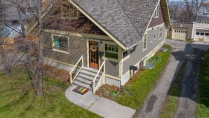 A two-story house with a steeply pitched roof, a front porch with a railing, and a front door with a wreath. - BozemanGetaways - Charming Condo Steps to Main (Bozeman)