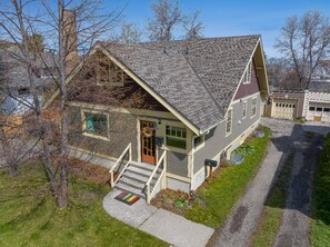 A two-story house with a steeply pitched roof, a front porch with a railing, and a front door with a wreath. - BozemanGetaways - Charming Condo Steps to Main (Bozeman)