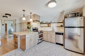 A modern kitchen with a central island, stainless steel appliances, and pendant lighting. - BozemanGetaways - Charming Condo Steps to Main (Bozeman)