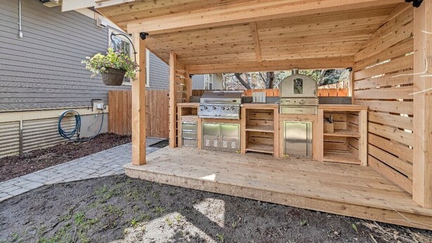 A wooden outdoor kitchen with a grill, built-in cabinets, and a hanging planter. - BozemanGetaways - Charming Condo Steps to Main (Bozeman)