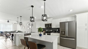 A modern kitchen with white cabinets, a central island with bar stools, stainless steel appliances, and pendant lighting.