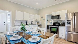 Een moderne keuken met witte kastjes, roestvrijstalen apparatuur en een eethoek met een houten tafel gedekt voor vier personen.