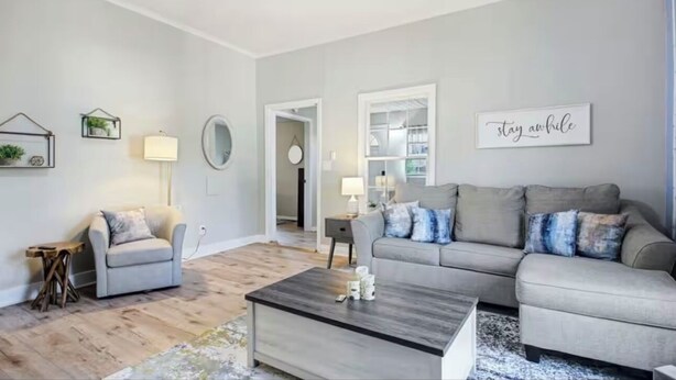 Een woonkamer met een grijze bank, een kleinere fauteuil, een salontafel en een boekenkast.