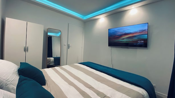 Ein modernes Hotelzimmer mit einem Bett, einem Schrank, einem Spiegel und einem Fernseher, der die Uhrzeit anzeigt.