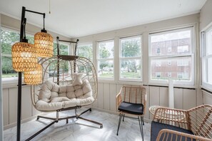 A room with a hanging chair, a wicker chair, and a floor lamp.
