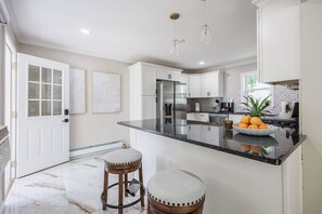 Una cocina moderna con armarios blancos, encimera de mármol y una isla central con taburetes.