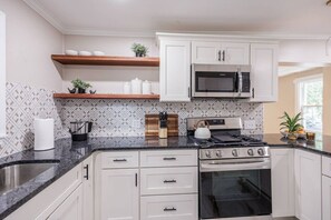 Una cocina con gabinetes blancos, una estufa de acero inoxidable, un microondas y un salpicadero decorativo.
