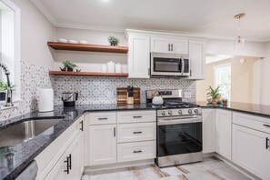 A modern kitchen with white cabinets, a stainless steel stove, a microwave, and a granite countertop.