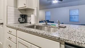 A kitchen with white cabinets, a granite countertop, a coffee maker, a sink, and a ceiling fan. - Walk to Downtown Edmond! Pet Friendly, Garage Access, King Bed! (Edmond)