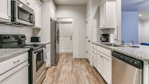 A modern kitchen with white cabinets, stainless steel appliances, and a wooden floor. - Walk to Downtown Edmond! Pet Friendly, Garage Access, King Bed! (Edmond)