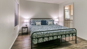 A bedroom with a bed, two bedside lamps, a ceiling fan, a window with blinds, and a door leading to a bathroom. - Walk to Downtown Edmond! Pet Friendly, Garage Access, King Bed! (Edmond)