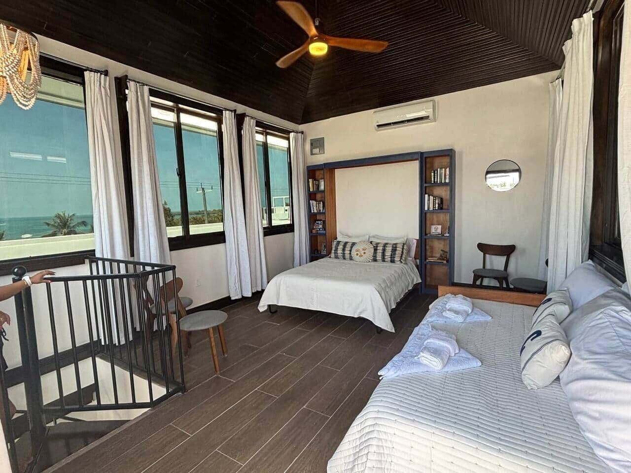Une chambre à coucher comprenant un lit, un bureau, une chaise, une bibliothèque et un balcon avec une balustrade.