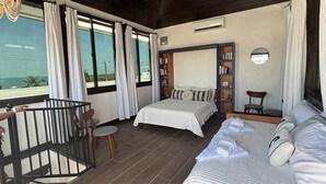 Ein Schlafzimmer mit einem Bett, einem Schreibtisch, einem Stuhl, einem Bücherregal und einem Balkon mit Geländer.