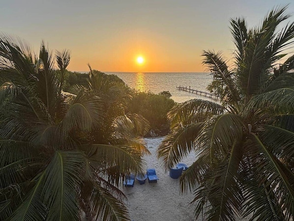 A beach scene with palm trees, a wooden pier, and a sunset.