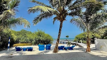 Une plage bordée de palmiers, avec des chaises longues bleues et une vue dégagée sur l’océan.