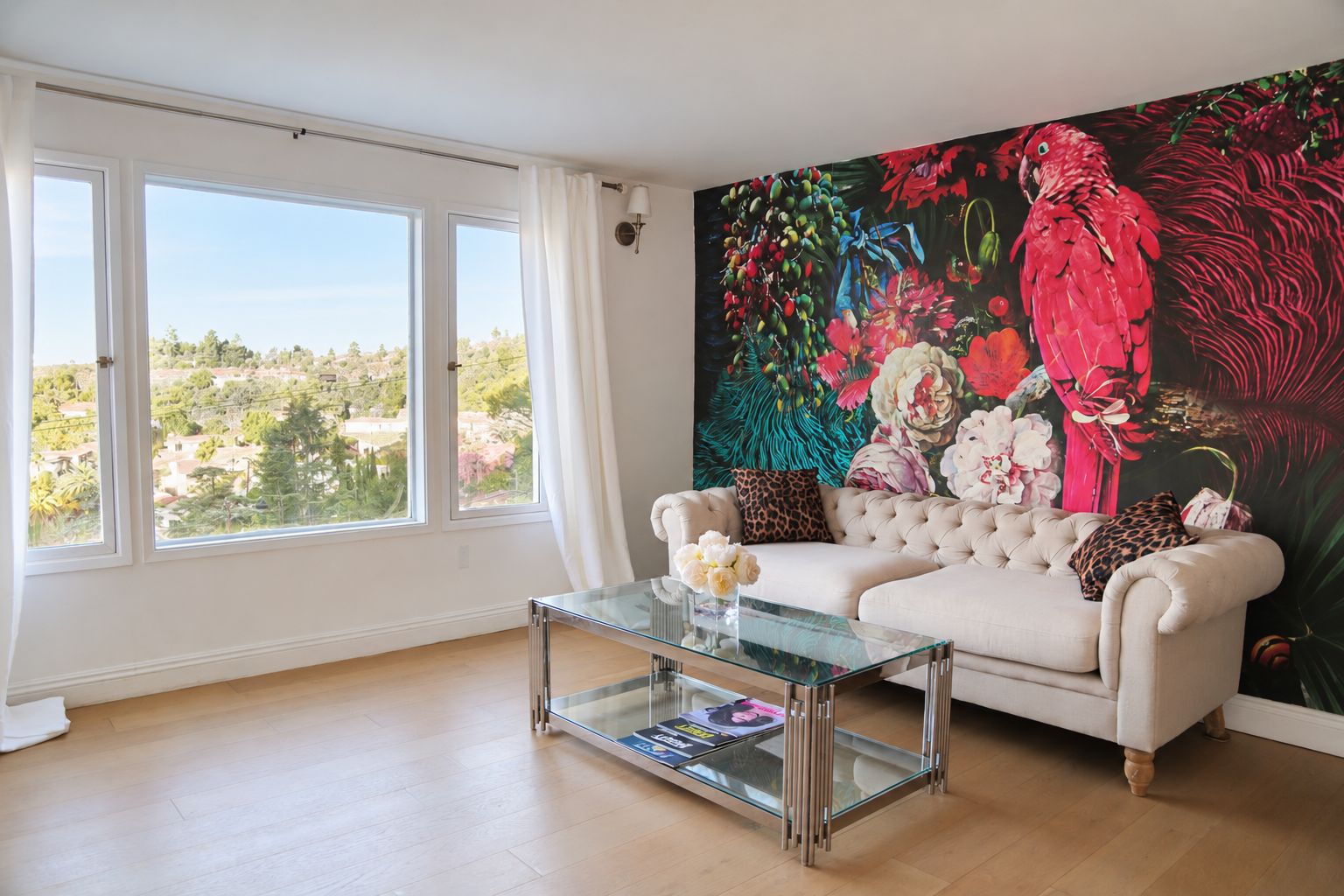 Un salon avec un canapé, une table basse en verre et une grande fresque murale à motifs floraux.