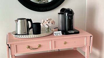 A pink vanity with a round mirror, a tray with a coffee maker, and a sign indicating no drinks allowed.