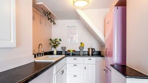A compact kitchen with white cabinets, a black countertop, a patterned floor, and a pink refrigerator. - Stunning 1-bedroom apartment with view (Glendale)