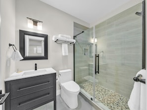 A modern bathroom with a glass-enclosed shower, a white toilet, a vanity with a mirror, and a towel rack.