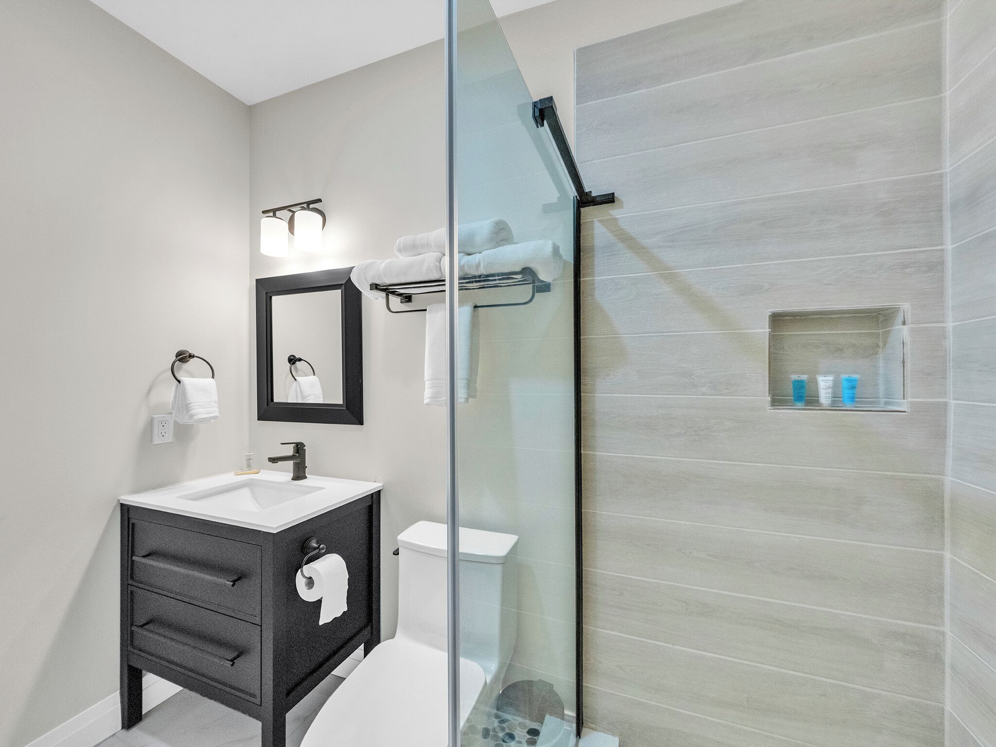 A modern bathroom with a glass-enclosed shower, a white sink, and a black vanity.